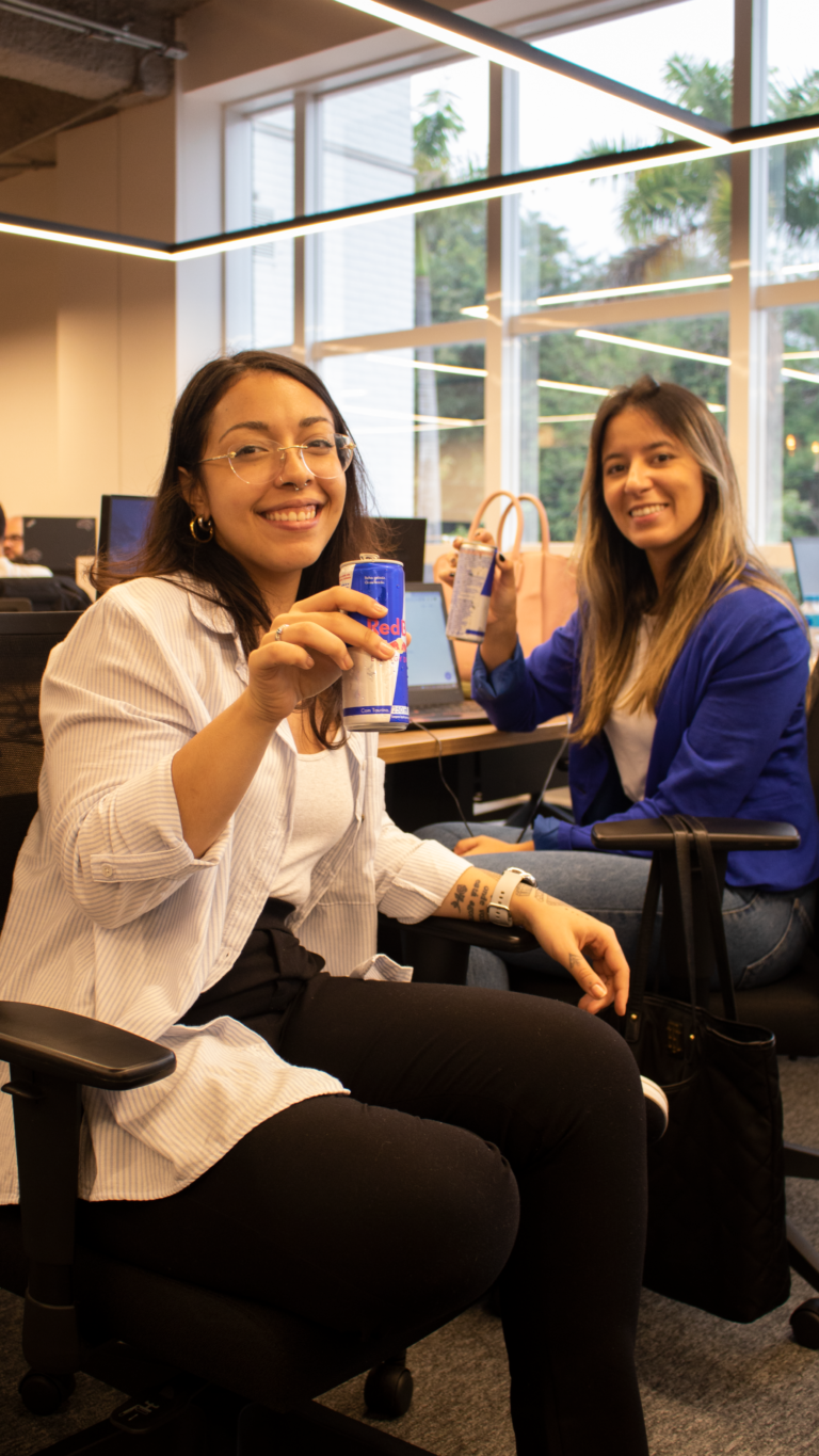 Duas mulheres brindando com energetico em um escritorio